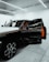 A luxury car is parked in a modern showroom with bright overhead lighting. The driver’s door is open, revealing a vibrant orange interior. The car's exterior features a sleek, black-and-white design with distinctive rims.