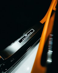 A close-up view of a vehicle's illuminated door sill, featuring the brand name 'Cullinan' prominently displayed against a sleek, metallic surface. The image includes orange and black elements that suggest a luxurious and modern aesthetic.