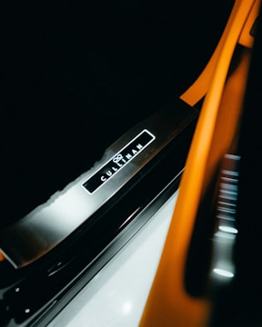 A close-up view of a vehicle's illuminated door sill, featuring the brand name 'Cullinan' prominently displayed against a sleek, metallic surface. The image includes orange and black elements that suggest a luxurious and modern aesthetic.