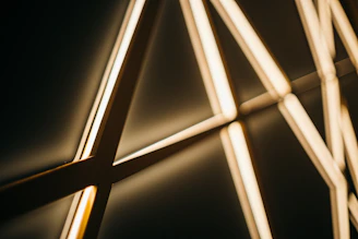 A close-up of delicate golden geometric lines softly glowing on a creamy white background.