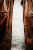 A close-up view of the torso area featuring a brown leather jacket with two zippered pockets, and underneath, a white textured knit sweater.