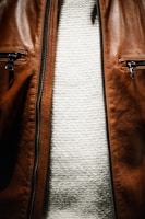 A close-up view of the torso area featuring a brown leather jacket with two zippered pockets, and underneath, a white textured knit sweater.