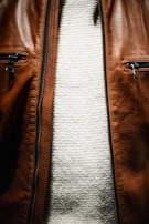 A close-up view of the torso area featuring a brown leather jacket with two zippered pockets, and underneath, a white textured knit sweater.