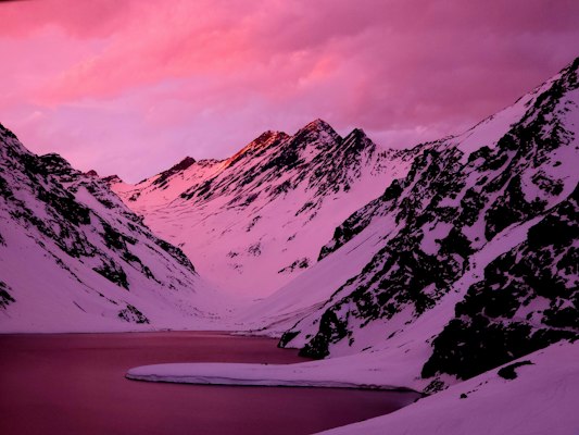 Pink alpenglow over snowy peaks and the frozen Laguna del Inca at Portillo