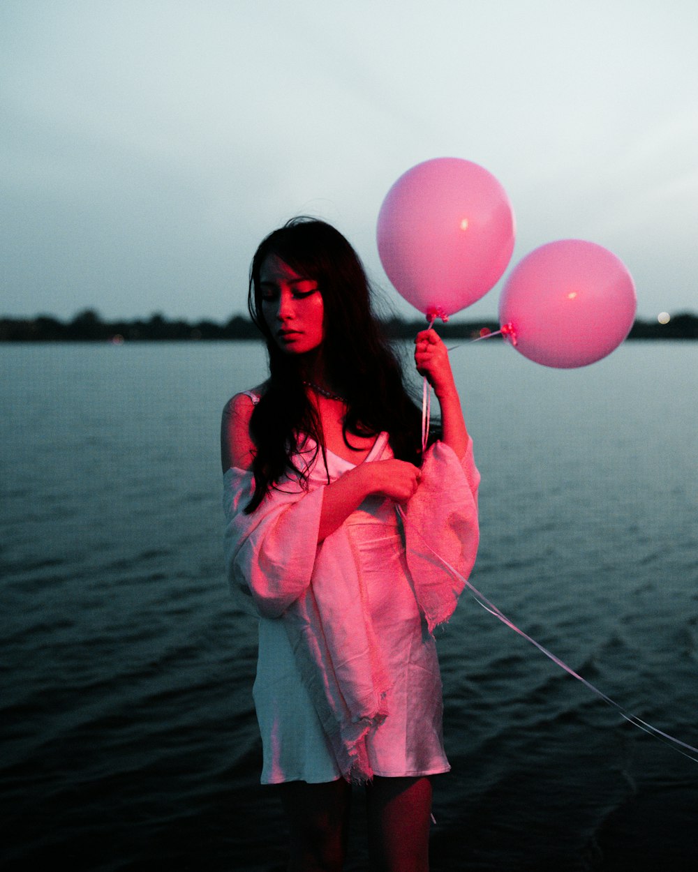 a woman in a white dress holding three pink balloons