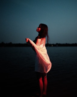 The weaver’s silhouette by twilight, the village glowing softly behind her, the tale of absence in her stance.