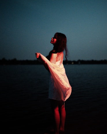 The weaver’s silhouette by twilight, the village glowing softly behind her, the tale of absence in her stance.