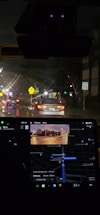 Nighttime inside a car with a visible dashboard displaying a GPS navigation system. The outside view through the windshield shows a street illuminated by traffic lights and car headlights. Road signs are visible, including a speed limit sign indicating 35 mph.