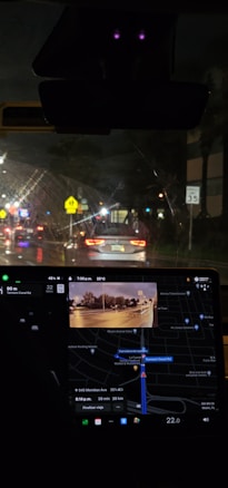 Nighttime inside a car with a visible dashboard displaying a GPS navigation system. The outside view through the windshield shows a street illuminated by traffic lights and car headlights. Road signs are visible, including a speed limit sign indicating 35 mph.