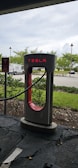Tesla charging station in a sunny outdoor parking lot with cars plugged in.