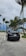 A black car parked on a sandy road with lush green palm trees and cloudy skies in the background.