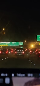 A night view of a highway with several vehicles heading south. Traffic appears congested as the cars' tail lights are visible. Overhead road signs indicate directions for highways 5, 118, and 210 South, along with Palmdale East. Streetlights on both sides illuminate the scene.