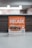 A promotional sign displaying a burger with layers of lettuce, tomato, and beef patty. The sign features the word 'Decade' in bold letters, promoting a contest with a QR code for participation. The background is softly blurred, highlighting the sign as the main focus.
