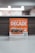 A promotional sign displaying a burger with layers of lettuce, tomato, and beef patty. The sign features the word 'Decade' in bold letters, promoting a contest with a QR code for participation. The background is softly blurred, highlighting the sign as the main focus.