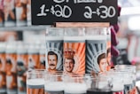 A variety of novelty prayer candles featuring illustrations of well-known figures with stylized backgrounds. They are displayed under a price sign offering them for sale with a special deal.