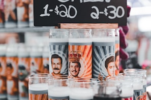A variety of novelty prayer candles featuring illustrations of well-known figures with stylized backgrounds. They are displayed under a price sign offering them for sale with a special deal.