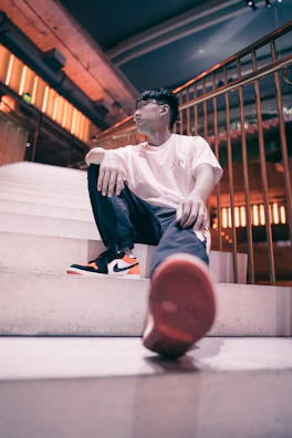 Model seated on concrete steps wearing the white t-shirt, blending urban vibe with simplicity.