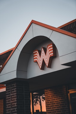 A building with a distinctive architectural design features a large orange and white stylized letter W logo under an arch. The structure is made of brick and stucco, and the lighting suggests it is either sunrise or sunset.