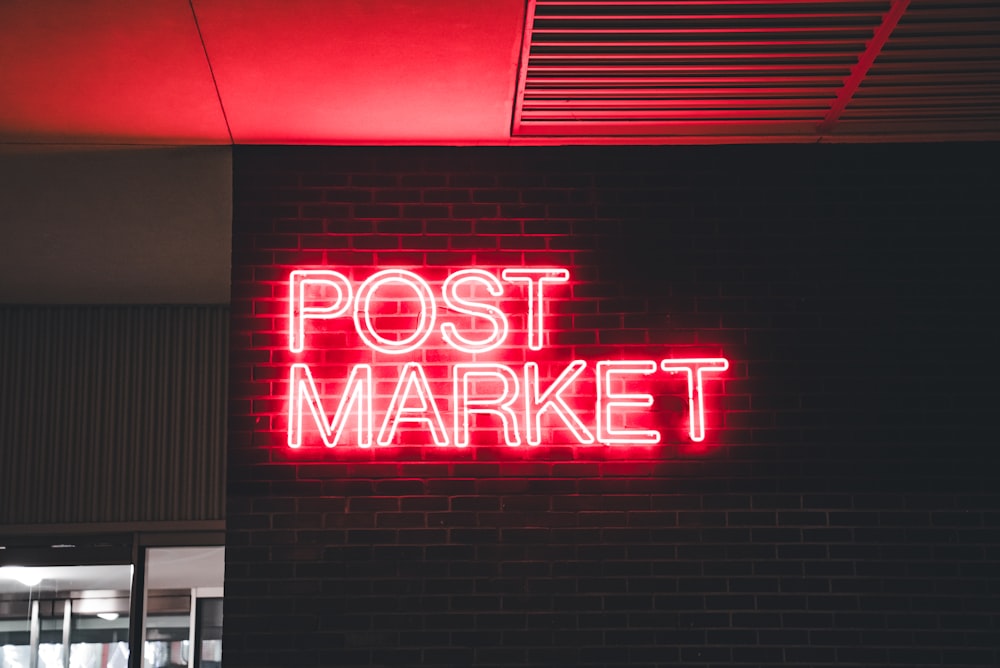 a neon sign that reads post market on a brick wall