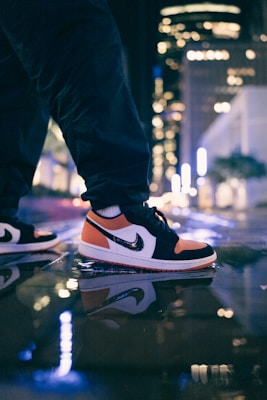 Streetwear sneakers in black and crimson red, captured mid-step on a rain-slicked urban street at night.