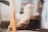 A white chicken standing on a wooden surface, with a slightly blurry background. The chicken is looking slightly to the side, and there is an out-of-focus object in the foreground, possibly a piece of wood or metal.