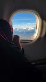 An elegant traveler gazing out from a glass-walled airplane cabin at a vast, cloud-streaked horizon.