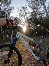A mountain biker adjusting their bike seat and handlebars on a trail at sunrise.