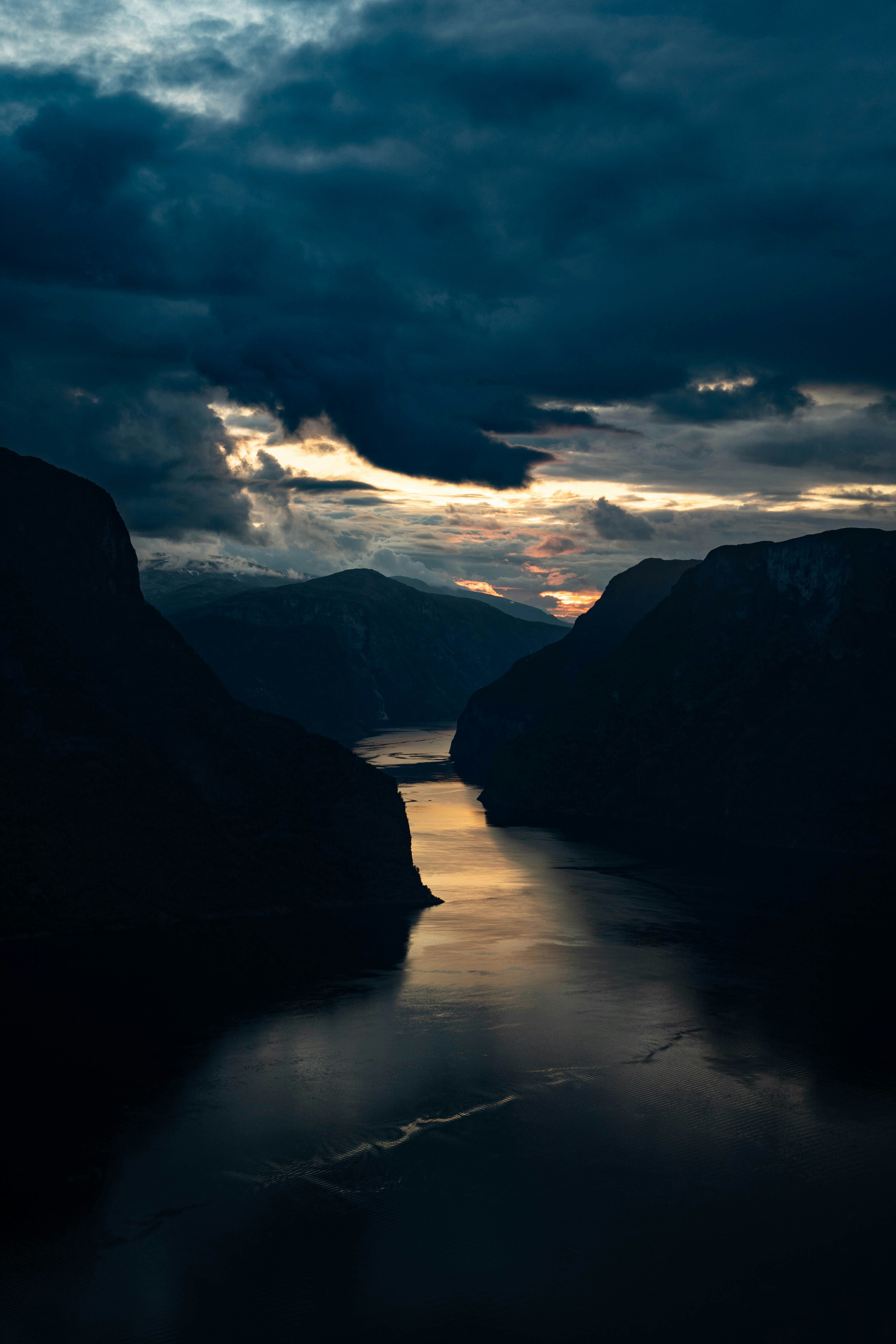 a body of water surrounded by mountains under a cloudy sky