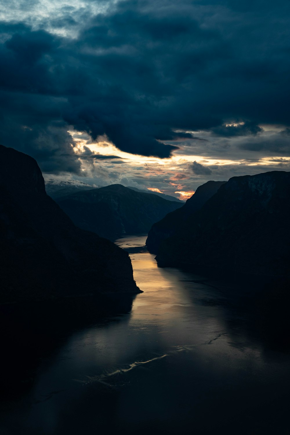 a body of water surrounded by mountains under a cloudy sky