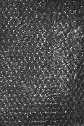 A textured surface of transparent bubble wrap with evenly distributed small air-filled bubbles.