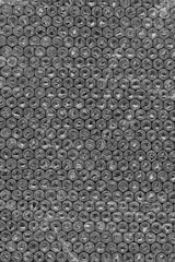 A close-up view of bubble wrap featuring a repetitive pattern of small, air-filled plastic bubbles arranged in neat rows and columns. The texture of the bubbles is semi-transparent and shiny.