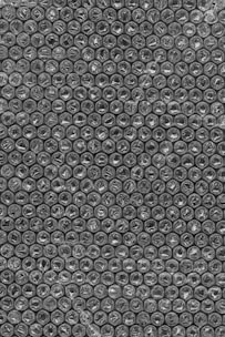 A close-up view of bubble wrap featuring a repetitive pattern of small, air-filled plastic bubbles arranged in neat rows and columns. The texture of the bubbles is semi-transparent and shiny.