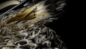 A complex, abstract digital artwork featuring swirling patterns and intricate details reminiscent of liquid metal. The image combines a mixture of gold, silver, and black hues, creating an almost three-dimensional appearance with reflective surfaces and smooth curves.