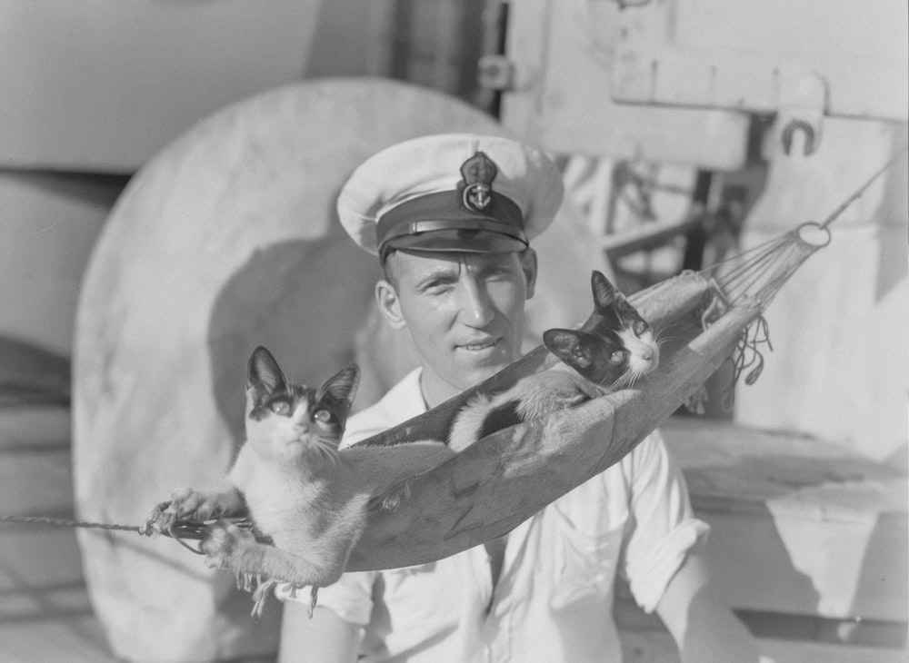 a man in a sailor's uniform holding two cats