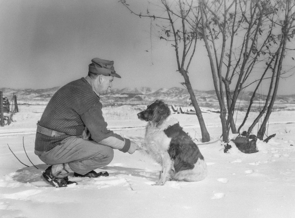 a man kneeling down next to a dog in the snow