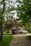 A gravel driveway surrounded by lush greenery leads to a small garage. Two vehicles, a black SUV and a white pickup truck, are parked in front of the garage. Overhanging trees with green leaves create a natural canopy over the scene.