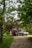 A gravel driveway surrounded by lush greenery leads to a small garage. Two vehicles, a black SUV and a white pickup truck, are parked in front of the garage. Overhanging trees with green leaves create a natural canopy over the scene.