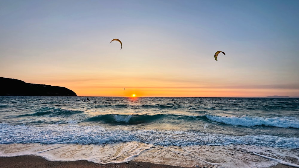 a couple of kites flying over the ocean at sunset