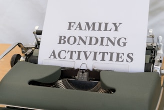 A typewriter with vintage design holding a sheet of paper that has the words 'FAMILY BONDING ACTIVITIES' typed in bold, black font. The typewriter is a dark green color, and the sheet of paper is positioned upright, indicating its recent use.