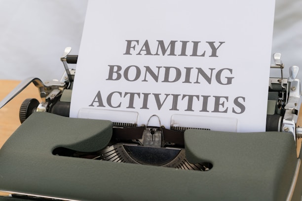 A typewriter with vintage design holding a sheet of paper that has the words 'FAMILY BONDING ACTIVITIES' typed in bold, black font. The typewriter is a dark green color, and the sheet of paper is positioned upright, indicating its recent use.