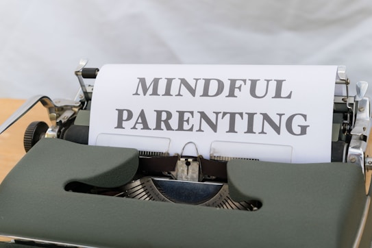 A vintage typewriter with a green body holds a sheet of paper displaying the words 'MINDFUL PARENTING' in bold, uppercase letters. The typewriter is placed on a light wooden surface, creating a classic and professional feel.