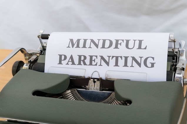 A vintage typewriter with a green body holds a sheet of paper displaying the words 'MINDFUL PARENTING' in bold, uppercase letters. The typewriter is placed on a light wooden surface, creating a classic and professional feel.