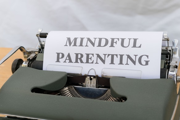 A vintage typewriter with a green body holds a sheet of paper displaying the words 'MINDFUL PARENTING' in bold, uppercase letters. The typewriter is placed on a light wooden surface, creating a classic and professional feel.