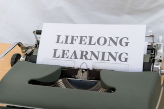 A typewriter with a sheet of paper displaying the words 'LIFELONG LEARNING' in bold letters. The typewriter appears vintage with a green cover, showcasing mechanical components around the paper.