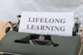 A typewriter with a sheet of paper displaying the words 'LIFELONG LEARNING' in bold letters. The typewriter appears vintage with a green cover, showcasing mechanical components around the paper.