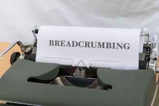 A vintage typewriter with a green casing is displaying a sheet of paper that has the word 'BREADCRUMBING' typed in bold uppercase letters. The typewriter is placed on a wooden surface, and the background appears to be a soft, neutral color.