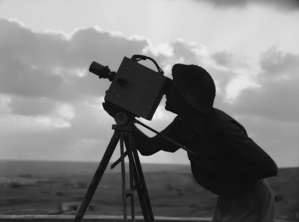 a black and white photo of a man looking through a telescope