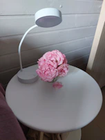 A minimalist bedside table featuring a sleek white lamp and a small vase with fresh flowers.