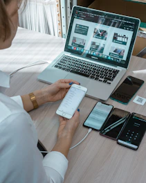 a woman sitting at a table with a laptop and cell phone