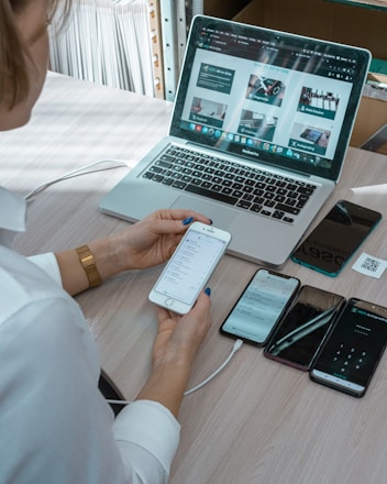 a woman sitting at a table with a laptop and cell phone